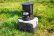The portable set with power station and electric coffee maker on the green grass. The cooking coffee outdoors or during the blackout.