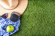 Spring, summer picnic, outdoor recreation background. A woman's straw hat, a picnic blanket or tablecloth, sunscreen spray, an apple on a background of green artificial grass or lawn, copy space