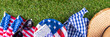 July 4, Independence Day traditional American picnic background. Plates, glasses, USA flags on green lawn or meadow grass, with blanket or tablecloth for picnic, sunglasses, copy space top view