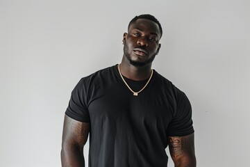 A poised young African-American man wearing a black t-shirt and gold chain necklace against a white background, ideal for fashion and lifestyle concepts.