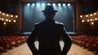 A lone figure in a suit and fedora stands with back to the camera looking out at the empty stage before him. posture exudes . .