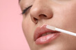 © New Africa - Woman applying lip gloss on pink background, closeup. Space for text