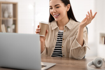 Poster - Young woman with cup of coffee using video chat during webinar at table in room