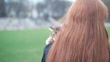 Teenage Girl With Red Beautiful Hair On The Street. On The Girl's Shoulder There Is A Small, Calm Kitten
