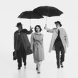 © master1305 - Black and white image of young beautiful smiling woman walking while tow man on background proposing her their umbrella. Concept of retro and vintage, fashion, relationship, emotions
