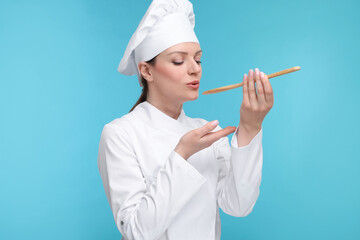 Canvas Print - Woman chef in uniform tasting something on light blue background