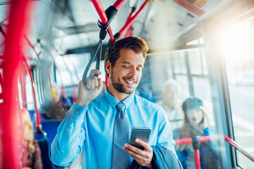 Smiling young adult businessman using smartphone on the bus