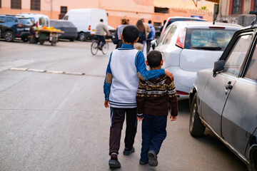 Two brothers walk down street, older one affectionately embracing younger, view from behind, family love, authentic urban African landscape, daily activities