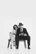 © master1305 - Monochrome portrait of young married couple, man in fedora hat and suit sitting with whisky glass and elegant smiling woman leaning on his shoulder. Concept of retro and vintage, romance, relationship