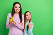© deagreez - Portrait of two people hold smart phone look indicate finger empty space isolated on green color background