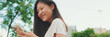 © Andrii Nekrasov - Happy beautiful brunette girl sitting on bench in city park, using phone with mobile app, surfing social media, checking news, Panorama