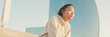 © Andrii Nekrasov - Asian girl in sportswear resting after workout sitting on steps on modern buildings background at sunrise, Panorama