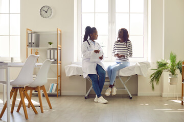 Wall Mural - Happy woman doctor talking with patient in hospital office. Patient and nurse radiate positivity, providing healthcare, creating an environment where medical expertise meets communication.