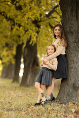 Wall Mural - Family day. Young mom and little daughter having fun and enjoy relaxing outdoors in autumn park. Adorable child girl tightly hugs and kiss her mother. Maternal care and love for kid. Mothers day