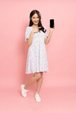 Fototapeta  - Young smiling Asian woman standing and showing blank screen mobile phone application isolated on pink background, Asian Thai model