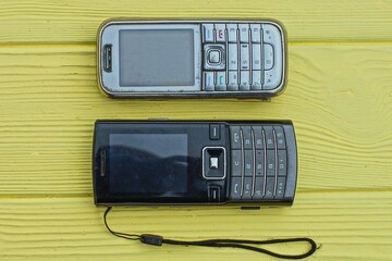 Wall Mural - two push-button plastic gray and black old mobile phones with batteries lie on a yellow wooden table