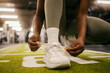 Close up of african american sportswoman's hands tying shoelace on sneaker at gym.