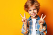 Little boy with a smiling happy face shows a peace sign with his fingers on bright blue background