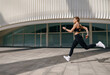 Young woman in sportswear is running on modern buildings background. Active lifestyle concept