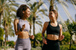 Two smiling women in sportswear are running on natural parkland background. Active lifestyle concept