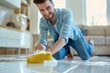 Kneeling man smiling while wiping floor tiles with a soapy yellow sponge