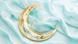 A golden crescent moon sculpture resting on a silky, wavy light blue fabric creating a serene and luxurious aesthetic.