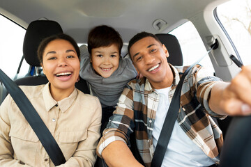 Excited family of three sitting in new car driving and enjoying road trip on vacation, parents and son posing and smiling at camera in auto