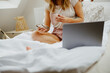 Close up of woman in comfort sleepwear using a laptop and cell phone on bed