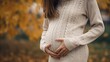 © Obsidian - a Close up of pregnant woman in sweater touching her belly in the autumn park.