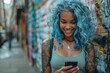 A young tattooed woman with blue hair smiles as she looks at her phone in an urban setting