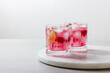 Raspberry drink with ice in a glass on a light background