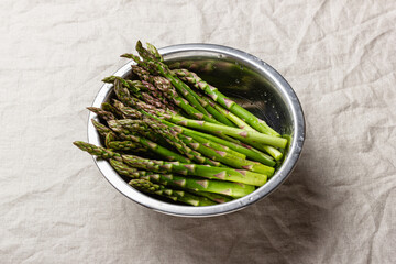 Wall Mural - Green asparagus in a metal bowl on a linen tablecloth