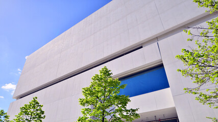 Wall Mural - Modern white concrete building walls against blue sky. Eco architecture. Green trees and concrete office building. The harmony of nature and modernity.