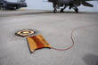 Electrical grounding cables are seen on a runway. Military fighter aircraft in the background.