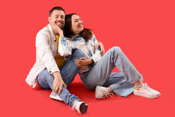 Wall Mural - Happy young couple sitting on red background