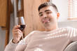Young man with glass of red wine sitting on sofa at home, closeup