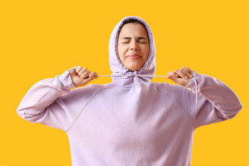 Wall Mural - Young woman in lilac hoodie on yellow background