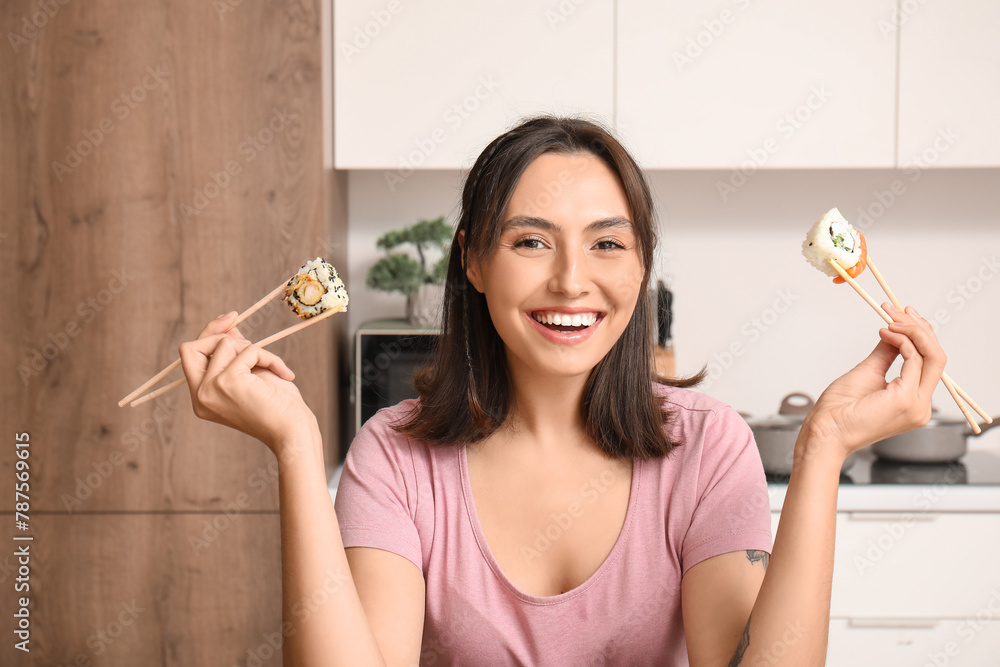 Happy young woman with tasty sushi rolls in kitchen