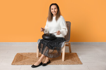 Canvas Print - Happy mature woman with sticks playing glucophone and sitting on chair near yellow wall