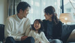 © MD Media - A young Japanese couple and their daughter, all smiling at the camera. Loving mother and father with kids enjoying time together at home sofa