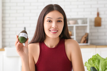 Poster - Beautiful young happy Asian woman with avocado at home. Keto diet concept