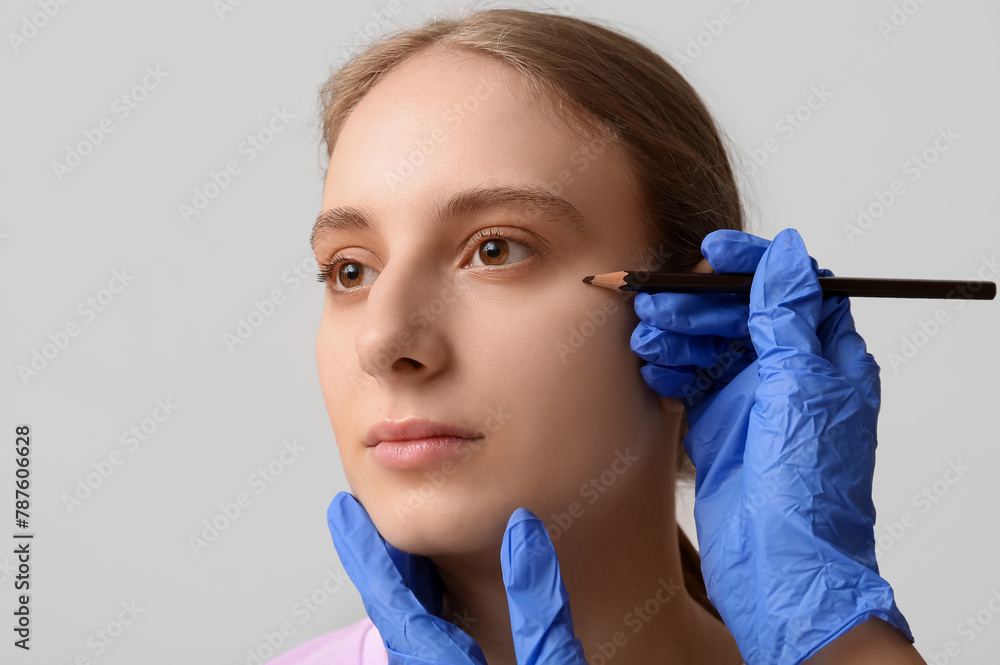 Plastic surgeon applying marks on female face against grey background, closeup. Blepharoplasty concept