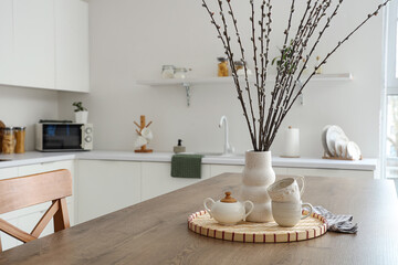 Wall Mural - Vase with willow branches and cups on table in kitchen, closeup