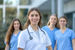 © Edvvin - Smiling female medical professional with stethoscope in foreground and colleagues behind