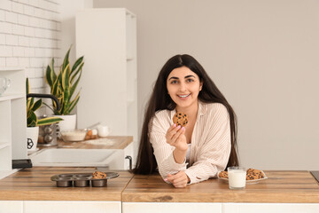 Canvas Print - Beautiful young woman holding tasty cookies with chocolate chips and glass of milk at home