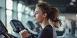 A woman is running on a treadmill in a gym. She is wearing a black shirt and has her hair in a ponytail