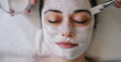 Young beautiful woman receiving white facial mask in spa beauty salon. Close-up view.