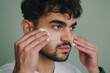 Young bearded caucasian man posing on isolated background with two round cotton pads. Man cleansing face with toner. Enjoying his fresh mouisturized face skin