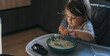 Little girl in the kitchen eagerly eating rice with a spoon independently.