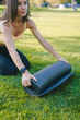 © Strelciuc - Pretty adult woman rolling her black yoga mat after a workout in the garden with green grass. Relaxation practicing yoga meditation outdoors, healthy lifestyle